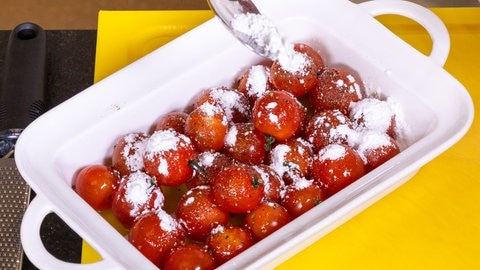 Ofengericht mit Tomaten, Burrata und Basilikum: Tomaten in einer servierfähigen Auflaufform mit Olivenöl, Salz und Pfeffer werden mit Puderzucker bestäubt.