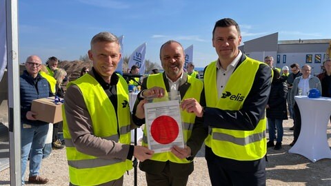 Landrat Ralf Lessmeister (CDU, links im Bild) übergibt die Baugenehmigung an den Geschäftsführer der Elis Wäscherei in Landstuhl, Jörg Scherf (Mitte) und den Projektmanager David Laczkowski.