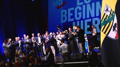 Funktionäre der AfD stehen bei der Wahlparty der AfD im Alten Theater vor dem Schriftzug "Es beginnt hier" auf der Bühne.