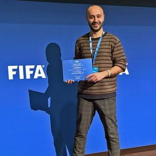Der Arzt Tarek Alhomsi vor einer FIFA-Fotowand