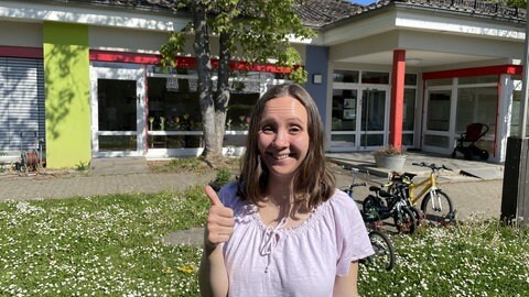 Lara Germer steht strahlend vor der Kita Flitz-Kids in Bretzenheim. Sie hält den Daumen hoch. 