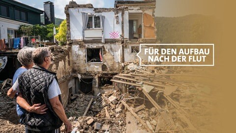 Sich umarmendes Paar schaut auf sein durch Hochwasser zerstörtes Haus in Rech an der Ahr