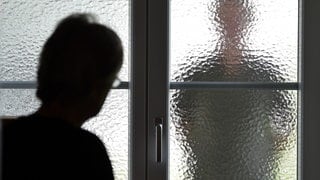 Eine Frau sieht den Schatten eines Mannes hinter einer Glastür. Wie können Stalking-Opfer geschützt werden?