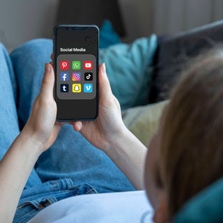 Ein Mädchen hält ein Smartphone auf dem ein Ordner mit diversen Social-Media-Plattformen zu sehen ist.