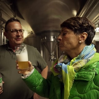 Sonja Faber-Schrecklein und Tobias Fischer stehen in einer Brauerei. Beide halten ein Bierglas in der Hand.