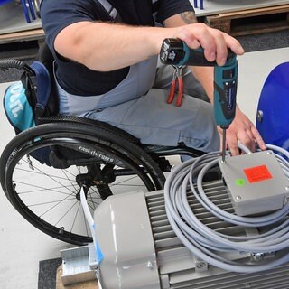 An einem Arbeitsplatz für Motorklemmen ist ein Mitarbeiter im Rollstuhl mit Montagearbeiten beschäftigt. (Symbolbild)