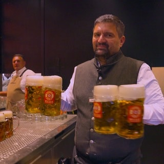 Ein Mann trägt mehrere Bierkrüge in einem Festzelt auf dem Cannstatter Wasen.