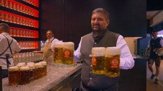 Ein Mann trägt mehrere Bierkrüge in einem Festzelt auf dem Cannstatter Wasen.