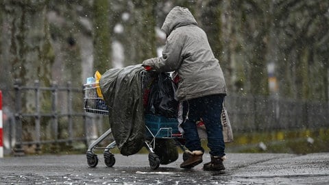 Eine obdachlose Frau schiebt ihr Hab und Gut in einem Einkaufswagen