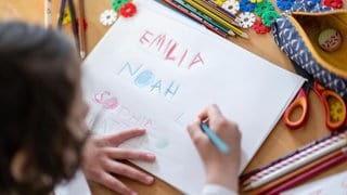 Ein Mädchen schreibt die Vornamen Noah, Emilia, Sophia und Mattheo auf ein Blatt. 