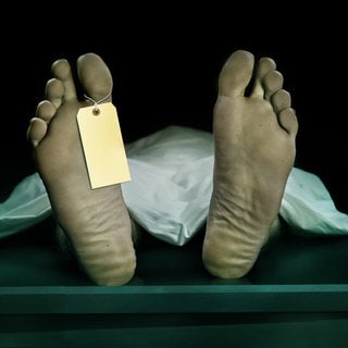Fußsohlen eines liegenden Toten, an einem Zeh hängt ein Zettel (Symbolbild): Kaum ein medizinischer Bereich ist so fehleranfällig wie die Leichenschau: Ärztinnen und Ärzte sind oft schlecht ausgebildet und übersehen immer wieder Verletzungen. 
