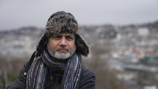 Faisal Khan trägt eine Fellmütze und eine Winterjacke. Er steht auf der Karlshöhe in Stuttgart, hinter ihm sieht man die Stadt.