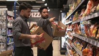 Safiullah ist Schichtleiter im Supermarkt. Er erklärt einem Kollegen etwas und zeigt auf ein Regal mit Chipstüten. 