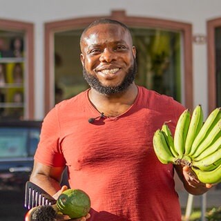 Junger Mann mit Bananen, Avocados und einem Kamm vor seinem Laden