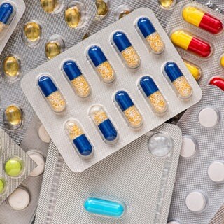 Es stapeln sich verschiedene Medikamentenverpackungen, in denen bunte Tabletten und Kapseln zu sehen sind. Für die Herstellung wird oft Gelatine aus Schlachtabfällen verwendet.
