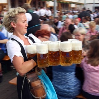 Servicekraft des Festzelts Löwenbräu stemmt Maßkrüge Bier und trägt sie von der Schänke zu den Tischen im Biergarten.