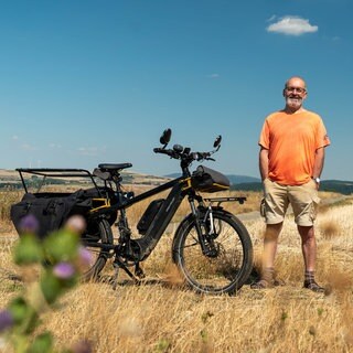 älterer Herr steht vor Trekkingrad in einem Feld