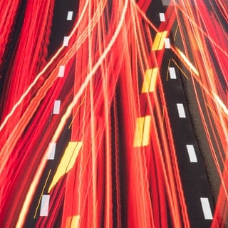 Die Scheinwerfer vorbeifahrender Fahrzeuge ziehen auf der Autobahn ihre Lichtspuren durch die hereinbrechende Dunkelheit 