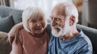Älteres Paar sitzt auf dem Sofa und umarmt sich