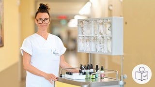 Pflegerin Manja Bergmann steht in einem Klinik·flur. Neben ihr steht ein kleiner Wagen. Auf dem Wagen stehen Fläschchen mit gut riechenden Ölen für ihre Arbeit. Rechts das SWR Logo für Leichte Sprache.