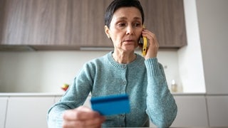 Eine Frau telefoniert und hält dabei eine Bankkarte in der Hand. In Mainz haben falsche Bankmitarbeiter mit einer neuen Betrugsmasche mehrere tausend Euro erbeutet