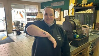Eine Frau hält lächelnd ihren Unterarm in die Kamera. Darauf ist ihr neues Tattoo: "Tal X" - das Logo der Gartenschau 2025.