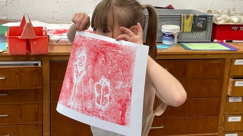 Ein Mädchen freut sich in der Jugendkunstschule Trier über sein selbstgemachtes Kunstwerk.