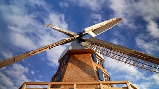 Eine Windmühle mit vier Flügeln und blauen Fensterläden. 