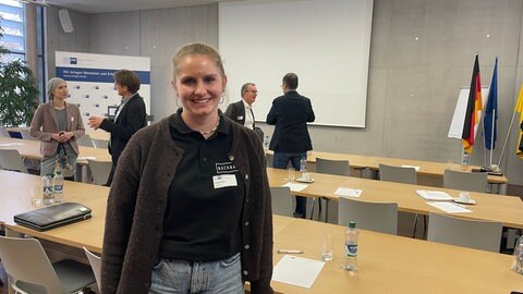 Helena Beck, eine junge Frau mit zurückgebundenen Haaren, lächelt in einem Vortragssaal der IHK in die Kamera. Im Hintergrund kleinere Grüppchen von Unternehmern im Gespräch. Es ging um die Frage, wie Firmen ihren Mitarbeitenden Wohnungen bieten können. 
