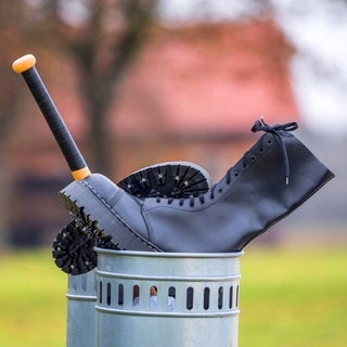 Springerstiefel und Baseballschläger im Abfalleimer als Symbolbild für den Ausstieg aus der rechten Szene: Extremisten einen Ausstieg aus ihrer Szene zu ermöglichen, ist aufwendig, der Erfolg vieler Ausstiegsprogramme ungewiss