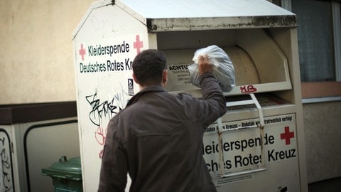 Ein Mann wirft einen Sack in einen Altkleidercontainer des DRK 