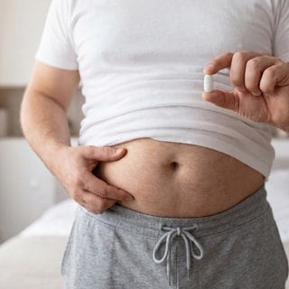 Anonymer Mensch mit Bauch und einer Pille zwischen den Fingern