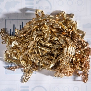 Der Goldkurs ist hoch, viele wollen ihr Gold zum Beispiel in Form von Schmuck verkaufen. Aber Vorsicht: Zahlreiche Goldhändler machen unfaire Angebote. Goldschmuck liegt auf einem Papier mit Statistiken.