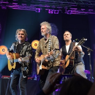 Die drei Musiker stehen mit jeweils einer Gitarre in der Hand auf der Bühne