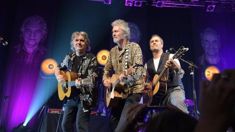 Die drei Musiker stehen mit jeweils einer Gitarre in der Hand auf der Bühne
