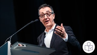 Minister·präsident Özdemir will das Bundes·land Baden-Württemberg voranbringen. Das Bild zeigt ihn an einem Redner·pult. Rechts das SWR Logo für Leichte Sprache. 