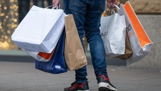 Mit vollen Einkaufstüten in den Händen geht ein Mann durch die Fußgängerzone.