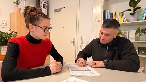 Ahmet Can und seine Sozialarbeiterin Y. Broghammer sitzen im Büro des Bezirksvereins für soziale Rechtspflege Mannheim.