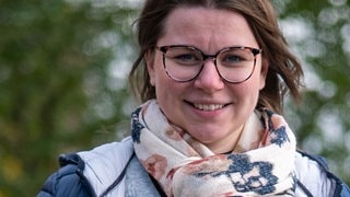 Junge Frau mit braunen Haaren, Melissa, steht vor herbstlichem Hintergrund
