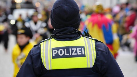 Polizist steht zum Schutz vor einem Fastnachtsumzug mit verkleideten Menschen