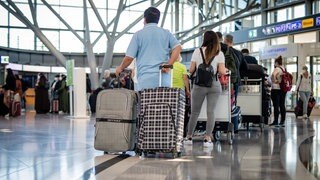 Reisende mit Koffern stehen an den Check-in-Schaltern am Flughafen Stuttgart Schlange.