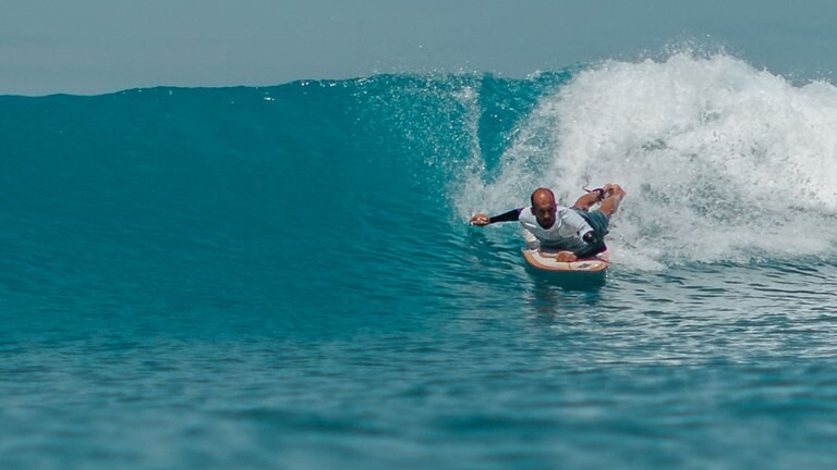 Der querschnittgelähmte Johannes Laing liegt auf seinem Surfbrett und reitet durch eine Welle.
