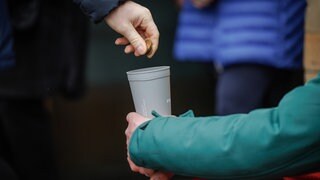 Eine Hand wirft Geld in einen Becher. Symbolbild: Armut in Ludwigshafen