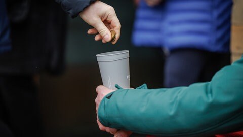 Eine Hand wirft Geld in einen Becher. Symbolbild: Armut in Ludwigshafen