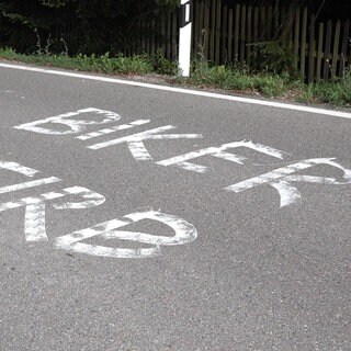 Auf einer Straße ist der Schriftzug "Biker stirb!" zu sehen.