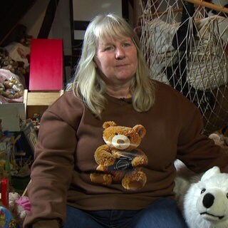 Claudia sitzt inmitten ihrer Teddybären. Sie trägt ein Teddybär-Shirt.