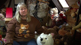 Claudia sitzt inmitten ihrer Teddybären. Sie trägt ein Teddybär-Shirt.