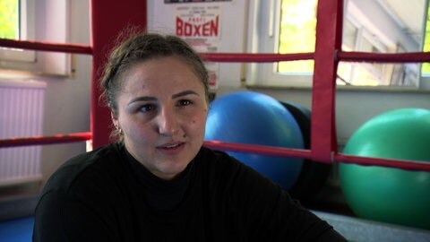 Boxerin Melina Maibaum sitzt vor dem Boxring. Im Hintergrund ist ein blauer Gymnastikball zu sehen.