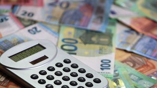 (Symbolbild) Ein Taschenrechner auf Geldscheinen: Die Stadt Baden-Baden will wegen der Finanzkrise weniger neue Schulden machen.