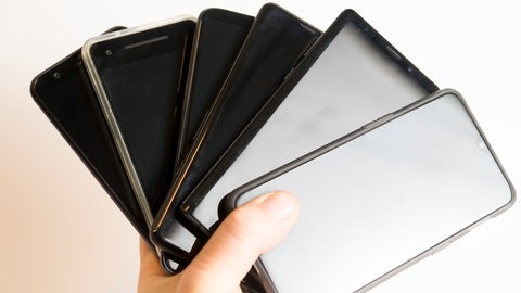 Alte Handys, die zuhause rumliegen in einer Hand, um dann Daten zu sichern, bevor das Smartphone entsorgt wird.